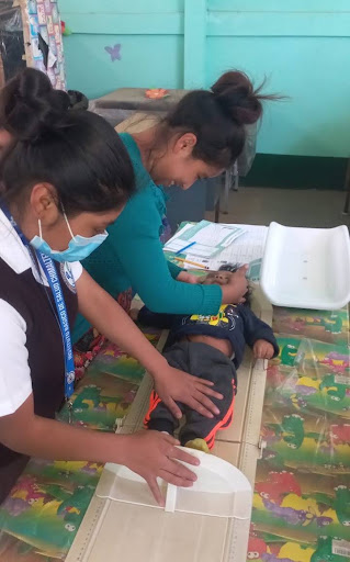 Two women position a baby on a measuring board while recording information.