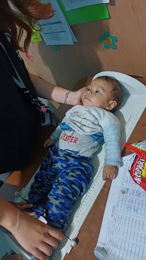 An infant lies on a measuring board while an adult positions the child’s legs for a length measurement.